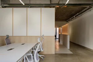 A minimalist office desk area with concrete walls and white tables.