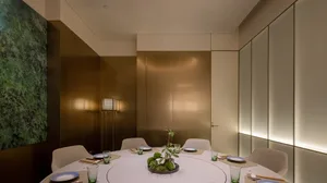 A modern, metallic-themed restaurant dining room with a circular table set for six, featuring a minimalist centerpiece and am