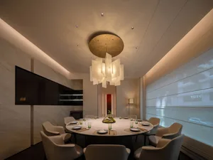 A modern restaurant dining room with minimalist design features, including a round table, chairs, and lighting fixtures.