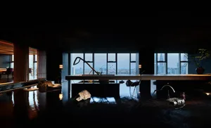 A minimalist hotel suite featuring a water feature with stones and a bird sculpture, overlooking a cityscape through large wi
