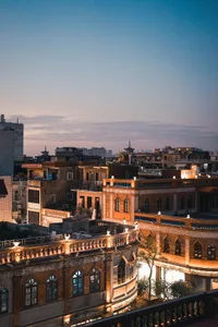 A cityscape featuring buildings made of brick and concrete, illuminated by warm evening light, under a sky transitioning from
