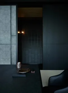 A minimalist Japanese-style room featuring dark wood paneling, a tatami mat, and traditional tea cup and tray on a dark table
