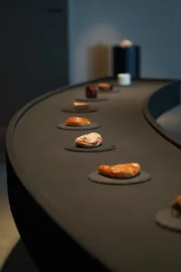 A black granite countertop featuring a conveyor belt with various types of pastries and breads.
