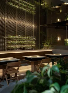 Modern restaurant interior with indoor plants, glass walls, and wooden furniture.