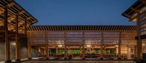Outdoor area of a modern restaurant featuring bamboo and wooden structures, with tables and chairs arranged under a large roo
