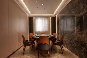 Modern dining room with marble flooring and walls, featuring a round table and orange chairs.
