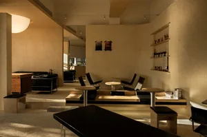 Modern restaurant interior with wooden and concrete seating, black leather accents, and minimalist design.