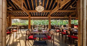 Modern restaurant interior with bamboo accents, featuring tables and chairs under a wooden beam ceiling with natural light.