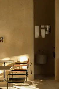 A minimalist interior with a concrete wall and floor, featuring modern furniture and a small mirror.
