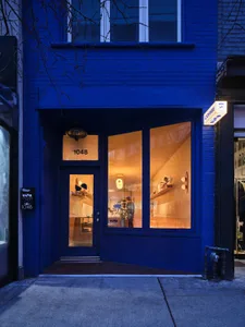 藍色店面搭配大型落地窗，透露出溫暖的室內燈光與燈具。