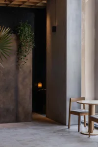 A contemporary restaurant interior featuring concrete walls and wooden furniture, with a single light fixture.