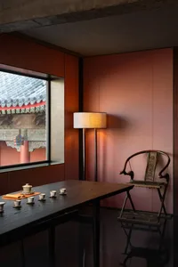 A modern tea room with a wooden table, fabric lamp, and traditional tea set, featuring a large window with an exterior view o