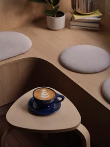 A cozy coffee shop interior with a wooden table featuring a blue ceramic coffee cup with latte art, surrounded by upholstered