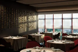 A restaurant interior featuring decorative Chinese calligraphy on the walls, round tables with tableware, and red chairs.