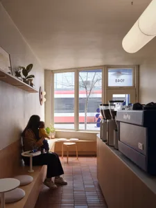 A minimalist cafe interior with wooden furniture and a view of a passing train through a large window.