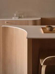 A modern, minimalist kitchen with wooden finishes and curved countertops.