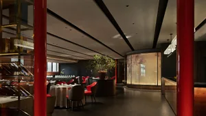 Lush luxury Chinese cuisine restaurant with tables set for service, red and black hues dominate the palette, and large potted