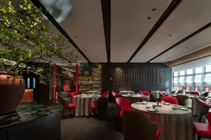 Modern restaurant interior with tables set for dining, red chairs, and a large tree in the corner.