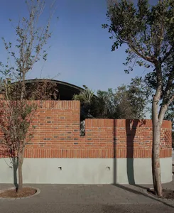 Modern exterior wall made of red bricks with green foliage growing on top and trees in the foreground.
