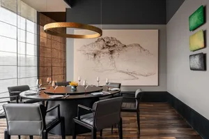 Modern dining room featuring a round table with chairs, wine glasses, and a mountain landscape painting.
