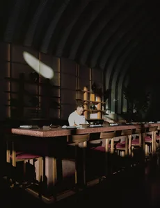 A chef preparing food behind a terrazzo counter in a restaurant interior with a dark, minimalist design.