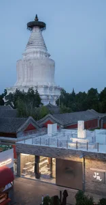 A white concrete stupa at night with surrounding trees and traditional Chinese-style buildings.