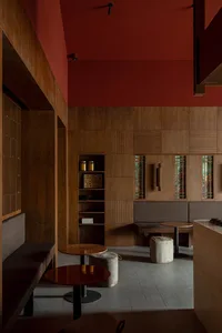 A minimalist restaurant interior featuring wood elements, with red walls, wooden benches, and round tables.