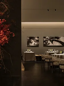 A modern dining room with tables arranged neatly, framed artwork depicting trees, and decorative elements such as yellow flow