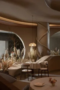 A modern restaurant interior with neutral textiles, featuring round tables, chairs, and decorative plants.