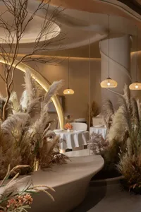 A modern restaurant interior featuring pampas grass and lighting.