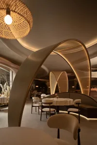 A modern restaurant with sleek, white walls, wooden tables, and fabric seating illuminated by soft lighting.