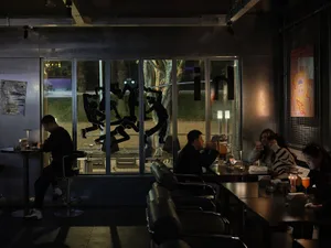 People sitting at tables in a modern metallic-themed cafe with large windows displaying outdoor scenery.