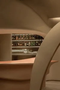 A modern bar with glass shelves displaying bottles of spirits and glasses.