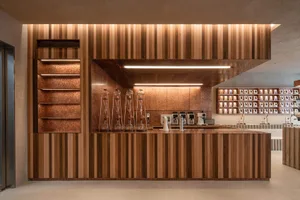 A modern, industrial-style coffee shop counter made of wood, featuring a striped design and various coffee-making equipment.