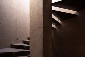 Concrete staircase with metal railings, illuminated by small sconces.