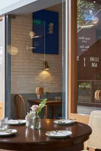 A cozy restaurant interior with wooden tables and chairs, a warm light fixture, and a brick wall.