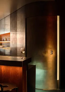A modern industrial bar with a metal-clad wall and a glass of wine on the counter.