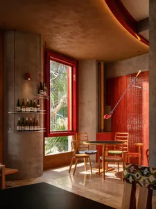 A modern restaurant interior featuring a concrete wall with a large window overlooking green foliage.