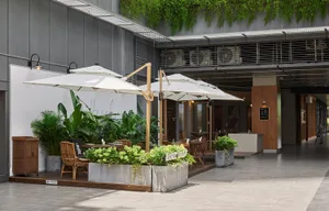 An industrial outdoor seating area with concrete tables, wooden chairs, and large umbrellas.
