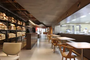 A spacious, industrial-style restaurant interior with concrete flooring, wooden furniture, and open seating.
