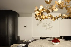 Modern dining room featuring a round marble table, elegant tableware, and a gold floral light fixture