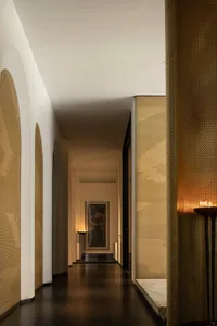 A modern interior corridor featuring a metallic perforated wall and candlelit ambiance.