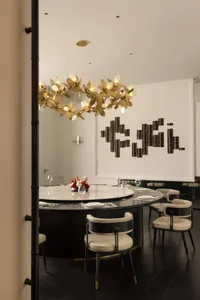 Modern restaurant dining room with metallic chandelier and circular table setup with chairs and wine glasses.