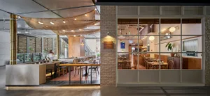 Modern restaurant interior with wooden tables, brick walls, and glass windows.