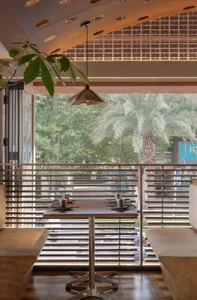 Cafe interior with wooden tables and chairs, large windows showing palm trees, and exposed brick wall