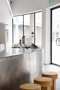 Modern coffee shop with minimalist design, featuring a metal counter and wooden stools.