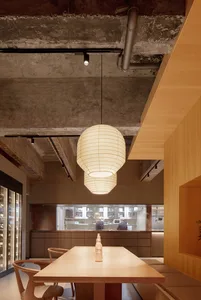 Modern restaurant interior featuring a dining area with wooden tables and chairs, concrete walls, and pendant lighting.