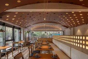 A modern restaurant interior featuring wooden tables, fabric seating, and perforated metal accents.