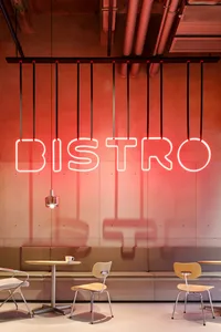 A minimalist industrial-style restaurant interior with exposed concrete walls, a red neon sign reading 'BISTRO', and simple s