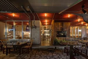 An industrial-style restaurant interior with concrete walls, wooden tables and chairs, and glass ceiling panels.